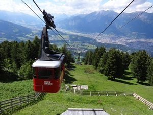 Cable car coming up mountain with view of valley in background in summer